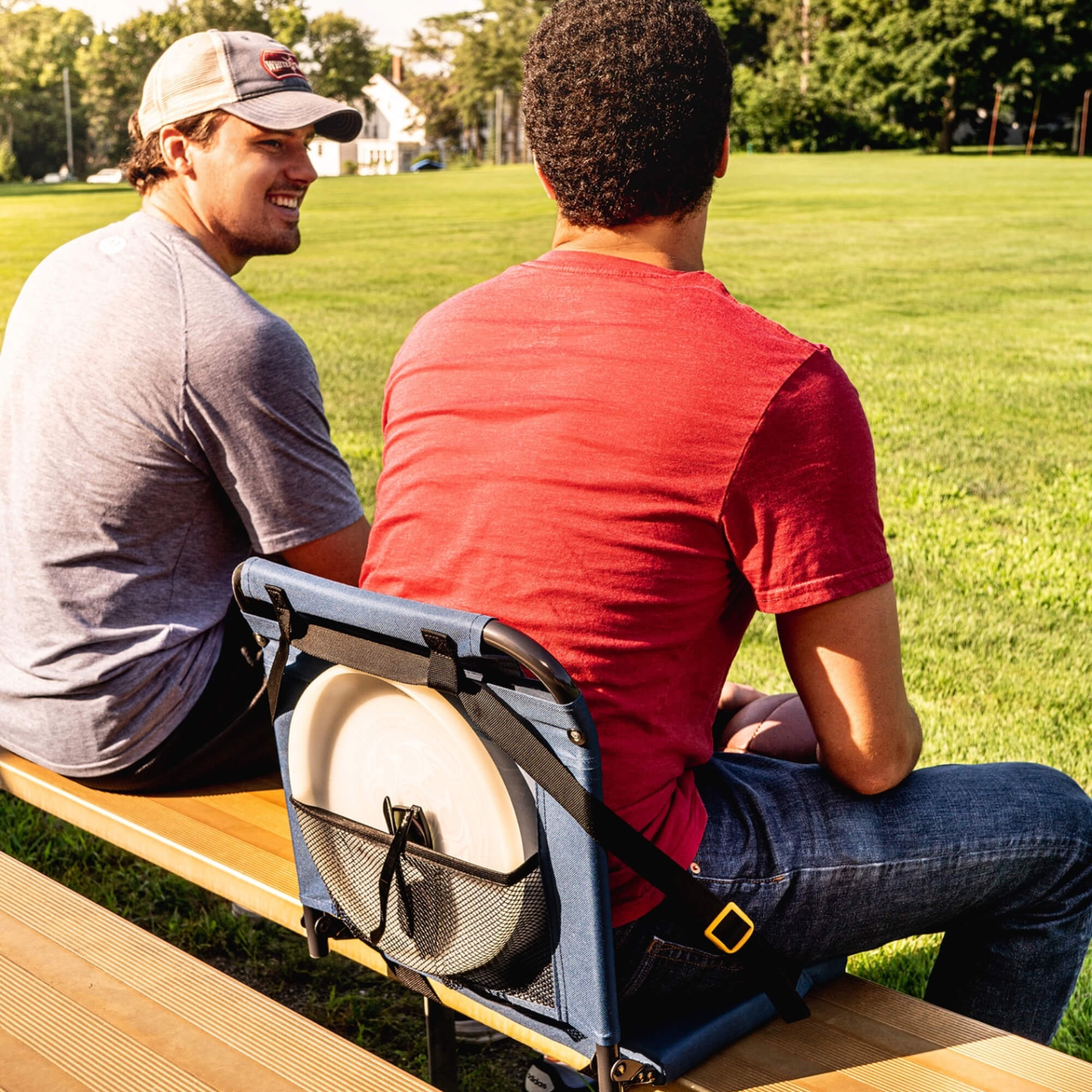 all-groups Two people sitting on bleachers; one uses a SitBacker seat with a frisbee stored in the mesh back pocket.