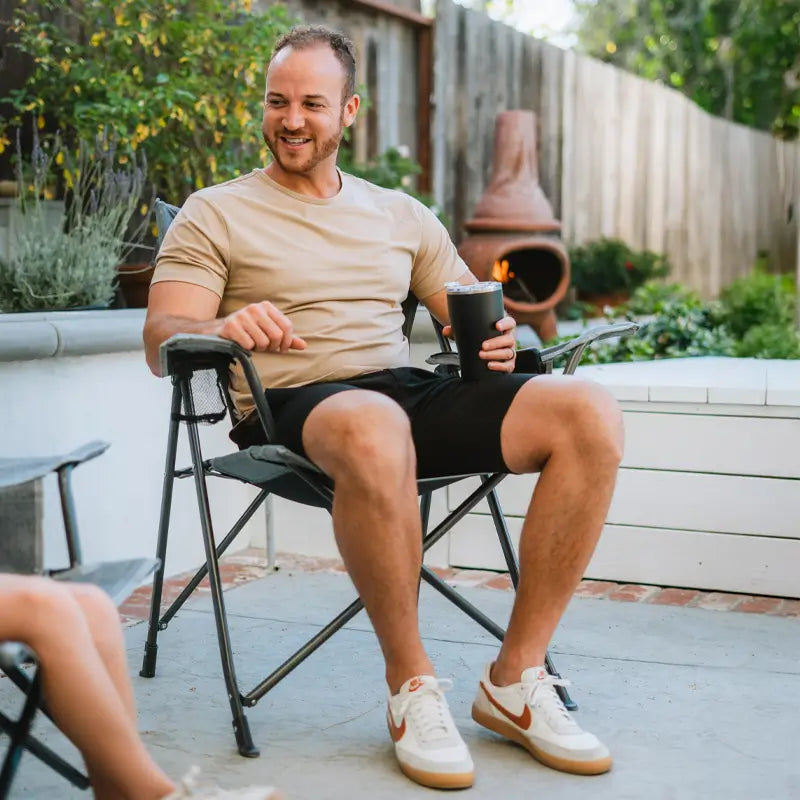 Man relaxing outdoors in a Comfort Pro Chair with a drink in hand, smiling in a backyard setting.
