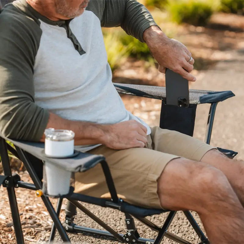 Man relaxing in the Heathered Charcoal Comfort Pro Rocker XL chair, placing a phone in the side pocket.