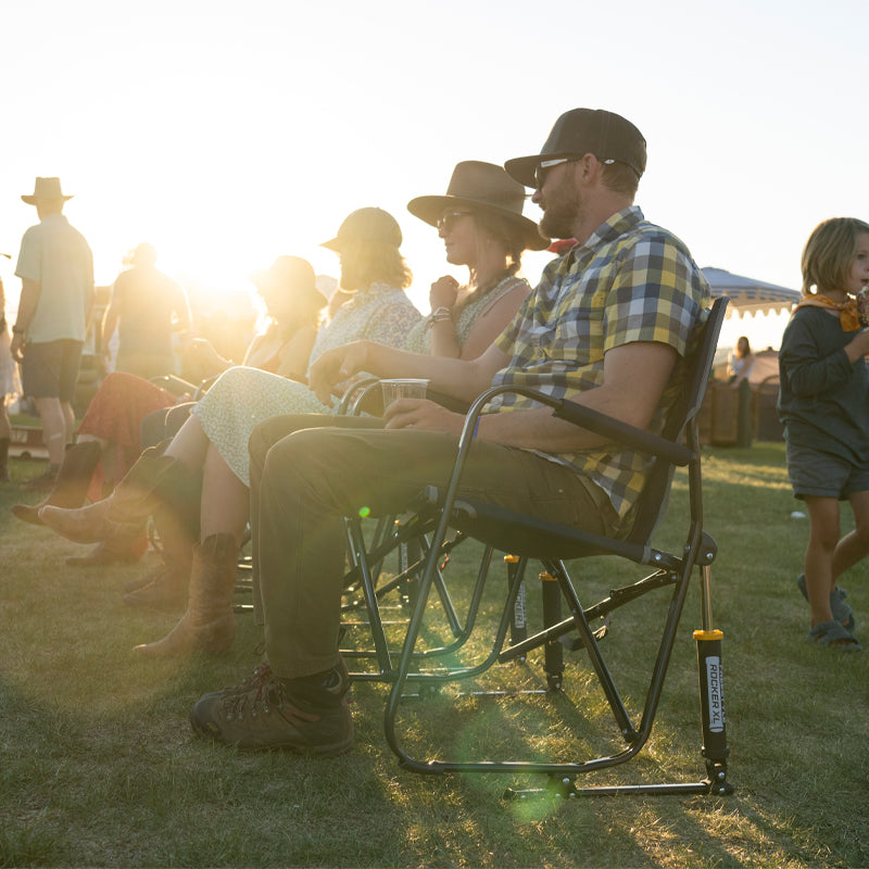 Group of people enjoying an outdoor concert seated in indigo Freestyle Rocker XL chairs at sunset.