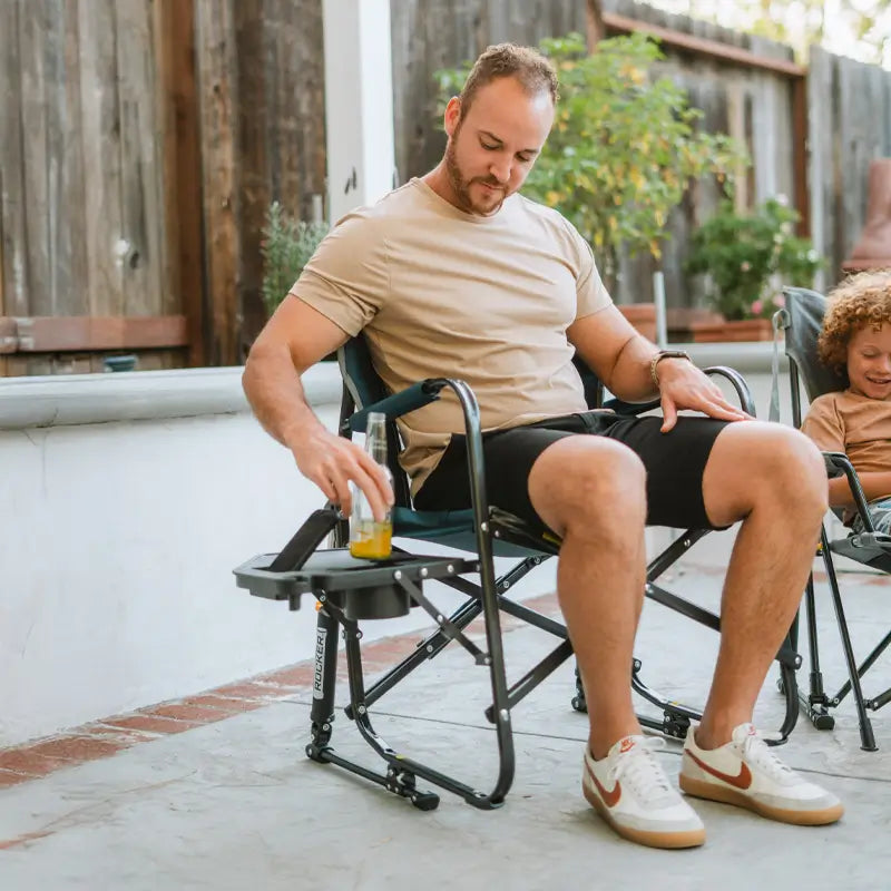 Man setting a bottle down on the Freestyle Rocker’s side table while sitting on a patio.