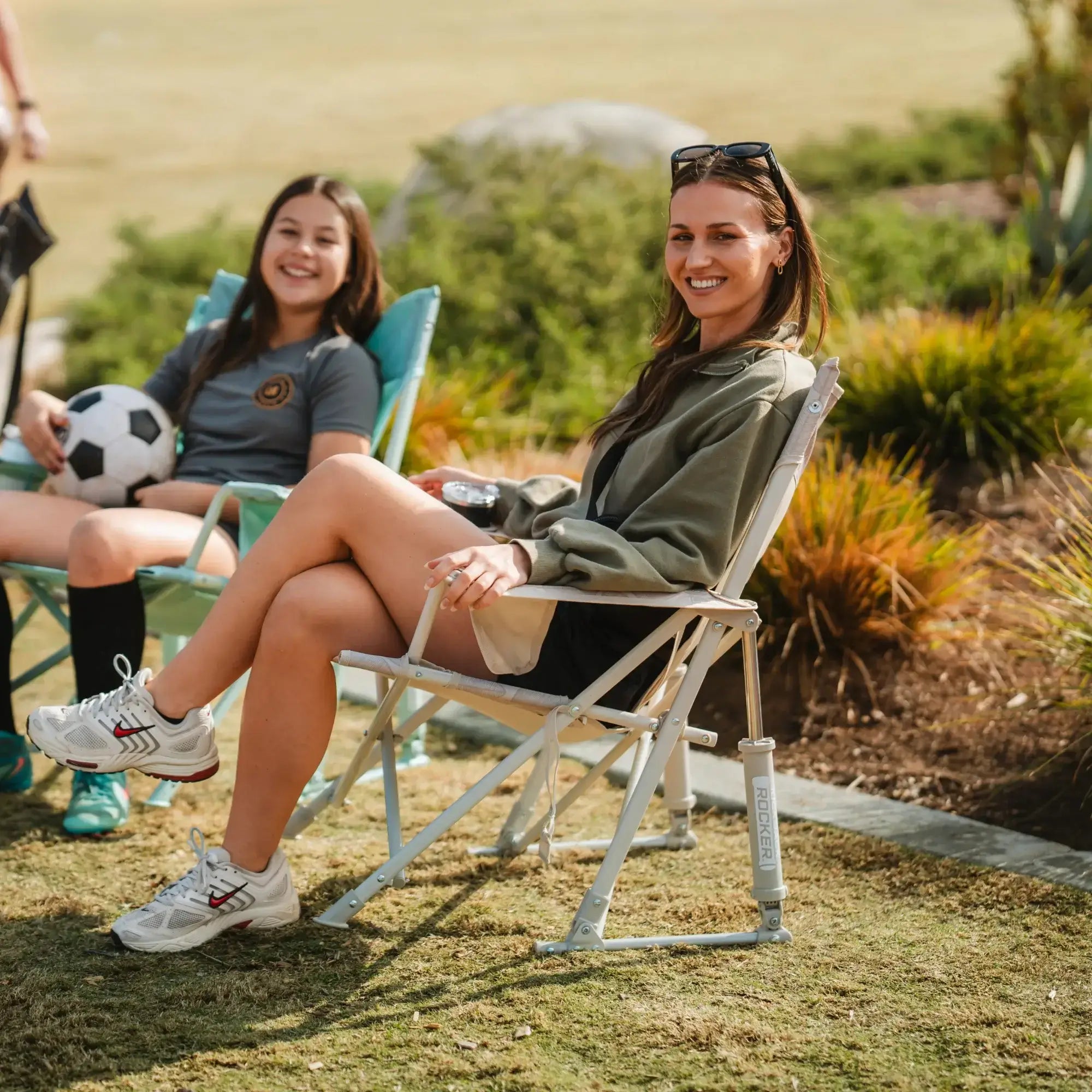 Two women sitting in comfort pro rockers watching a soccer game.