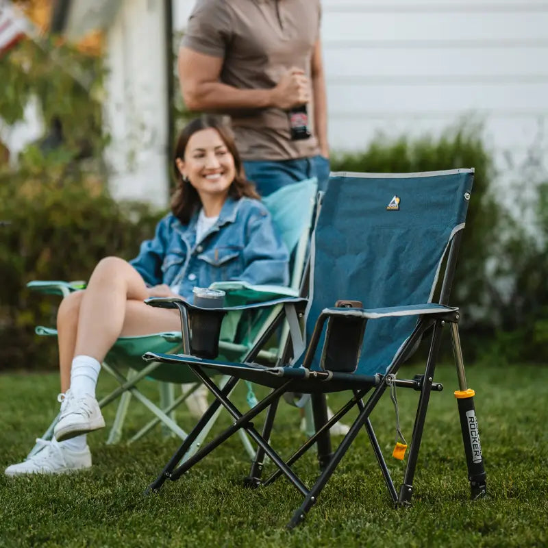 Heathered indigo Kickback Rocker on lawn next to seated woman and standing man at a casual gathering.