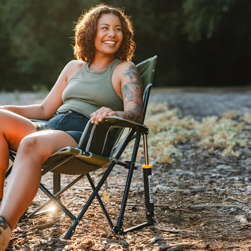 Woman smiling and relaxing in the heathered loden Kickback Rocker on a forest trail.