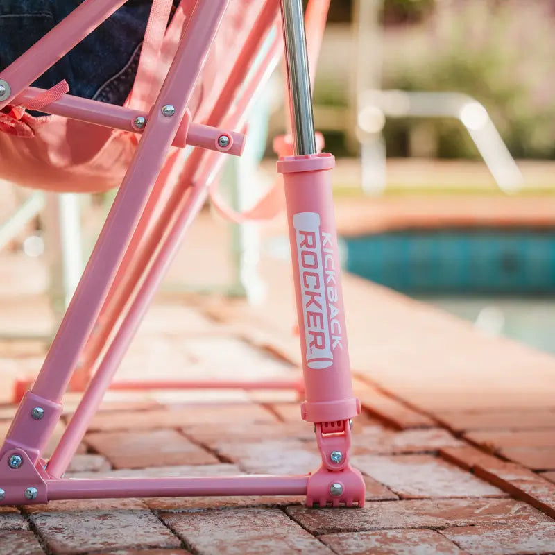 Side view of the Soft Pink Leaf Kickback Rocker’s rocker base and branding on patio bricks.
