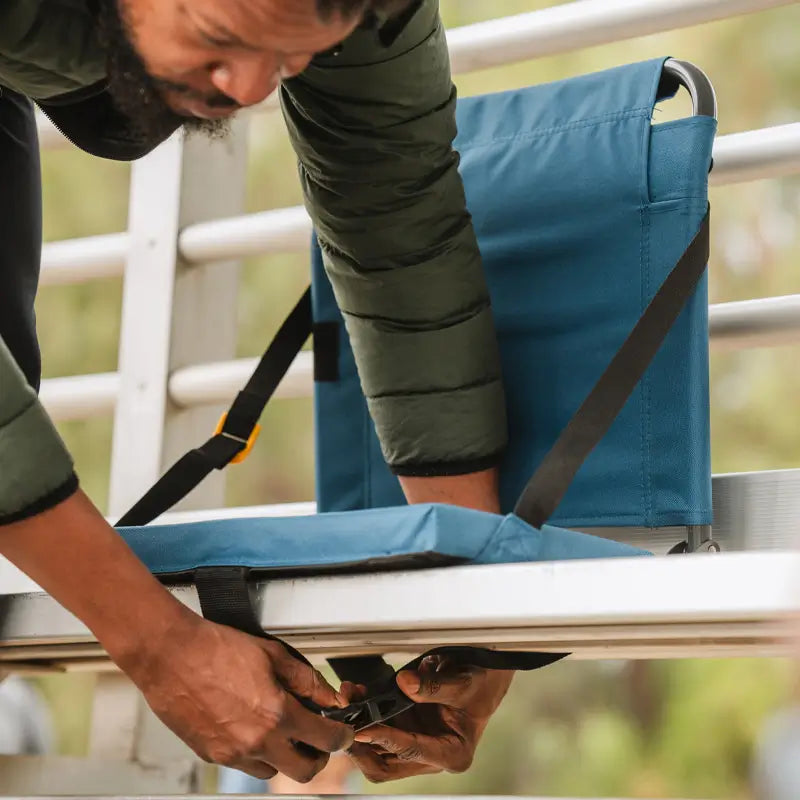 all-groups Person fastening the bottom strap of a SitBacker around a bleacher bench for added stability.