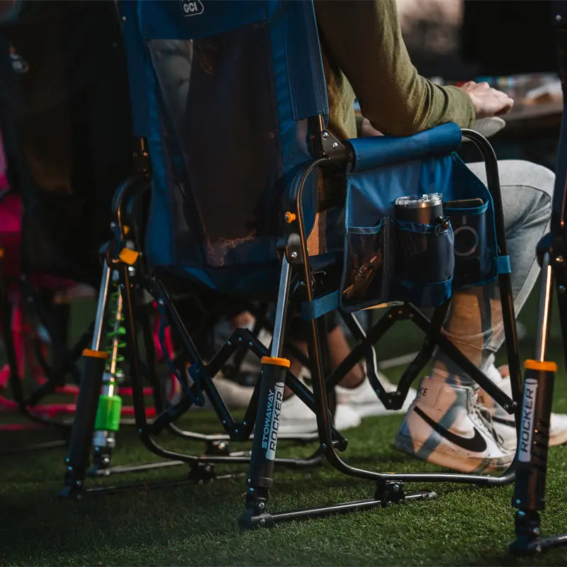 Close-up of the soft navy Stowaway Rocker with storage pockets holding a tumbler and gear at a night event.