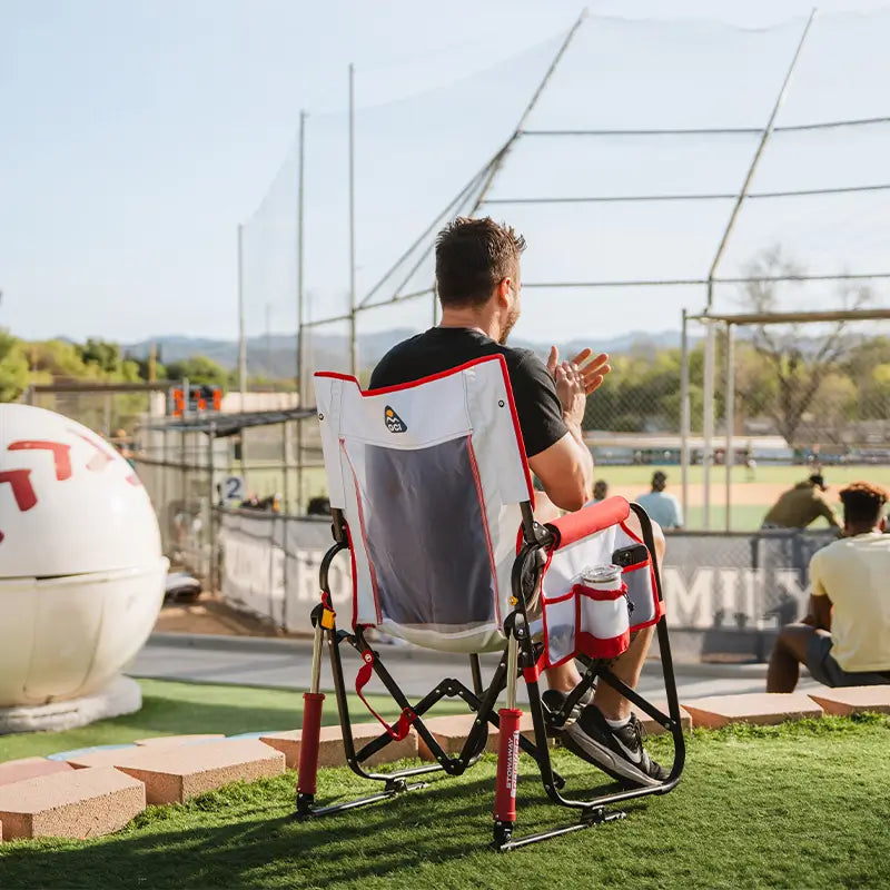 Person sitting in a sports chair on a baseball field with a large ball in the foreground.