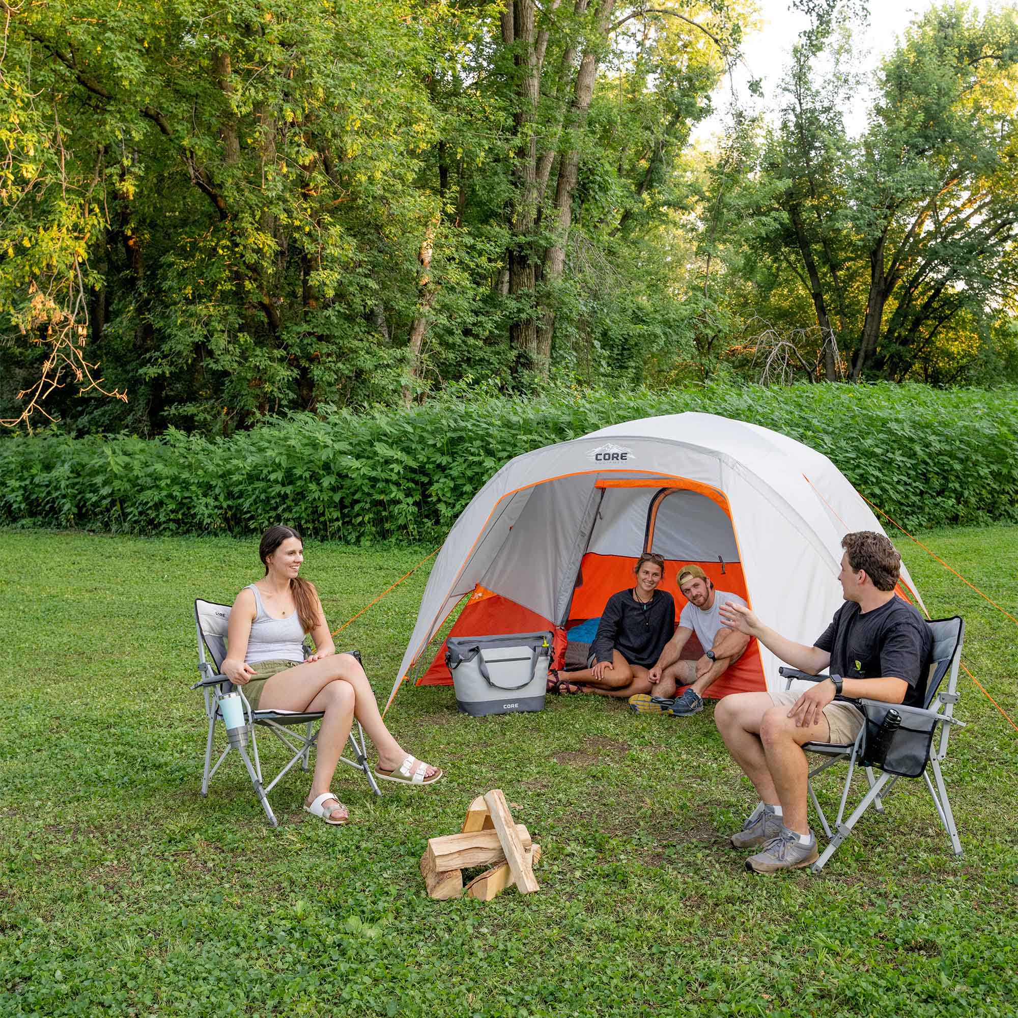 People camping outdoors with a CORE 6 person dome tent with vestibule in a wooded area.