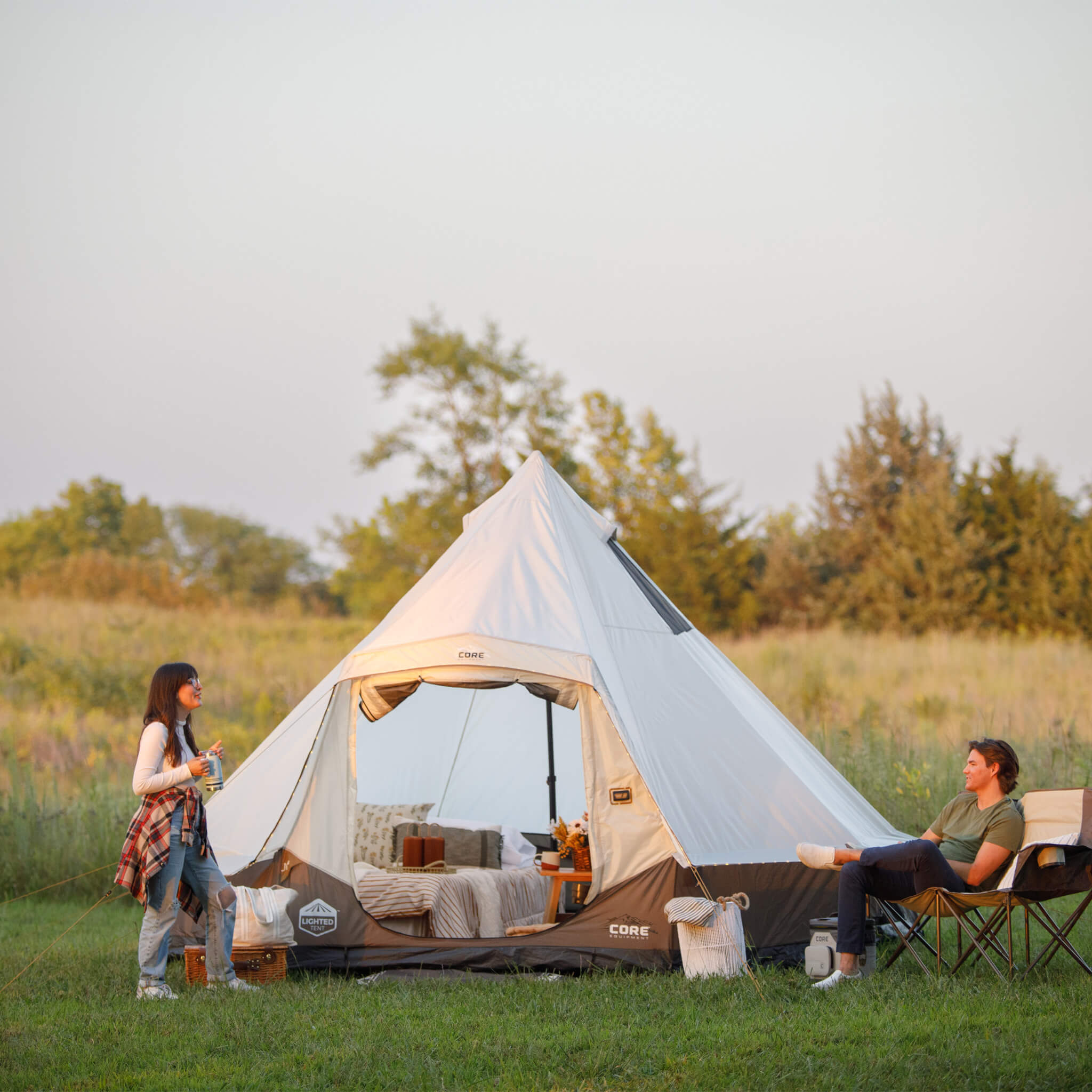 Family relaxing outside CORE 6 person lighted bell tent, shown set up in an open field with spacious design for camping.