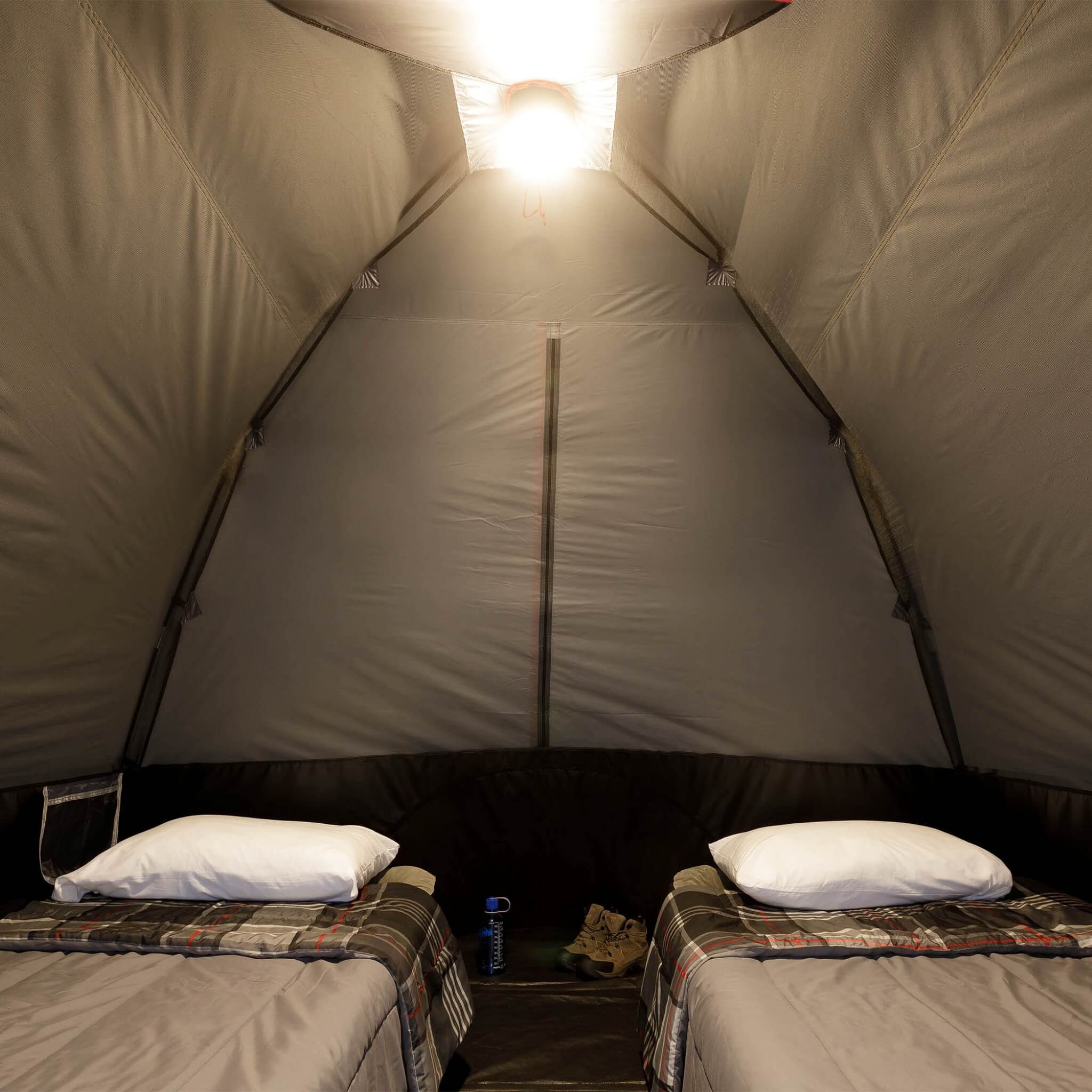 Inside view of CORE 6 person lighted dome tent with two cots, dark interior, and ceiling light on high mode providing overhead illumination.