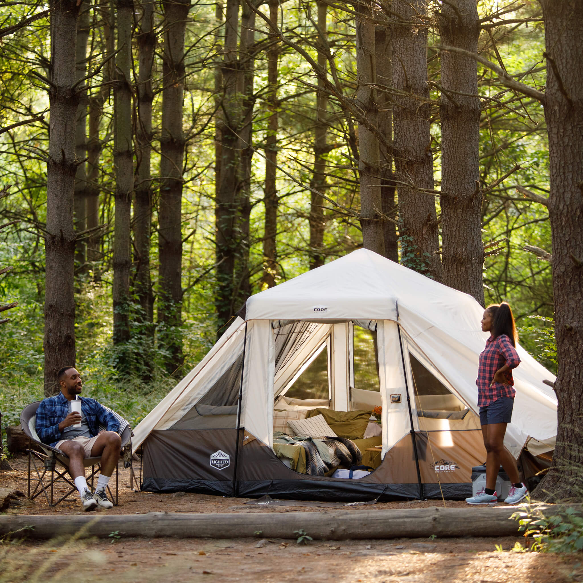 Family relaxing outdoors with CORE 6 person instant pyramid tent set up in wooded campsite, showing tall peak and space.