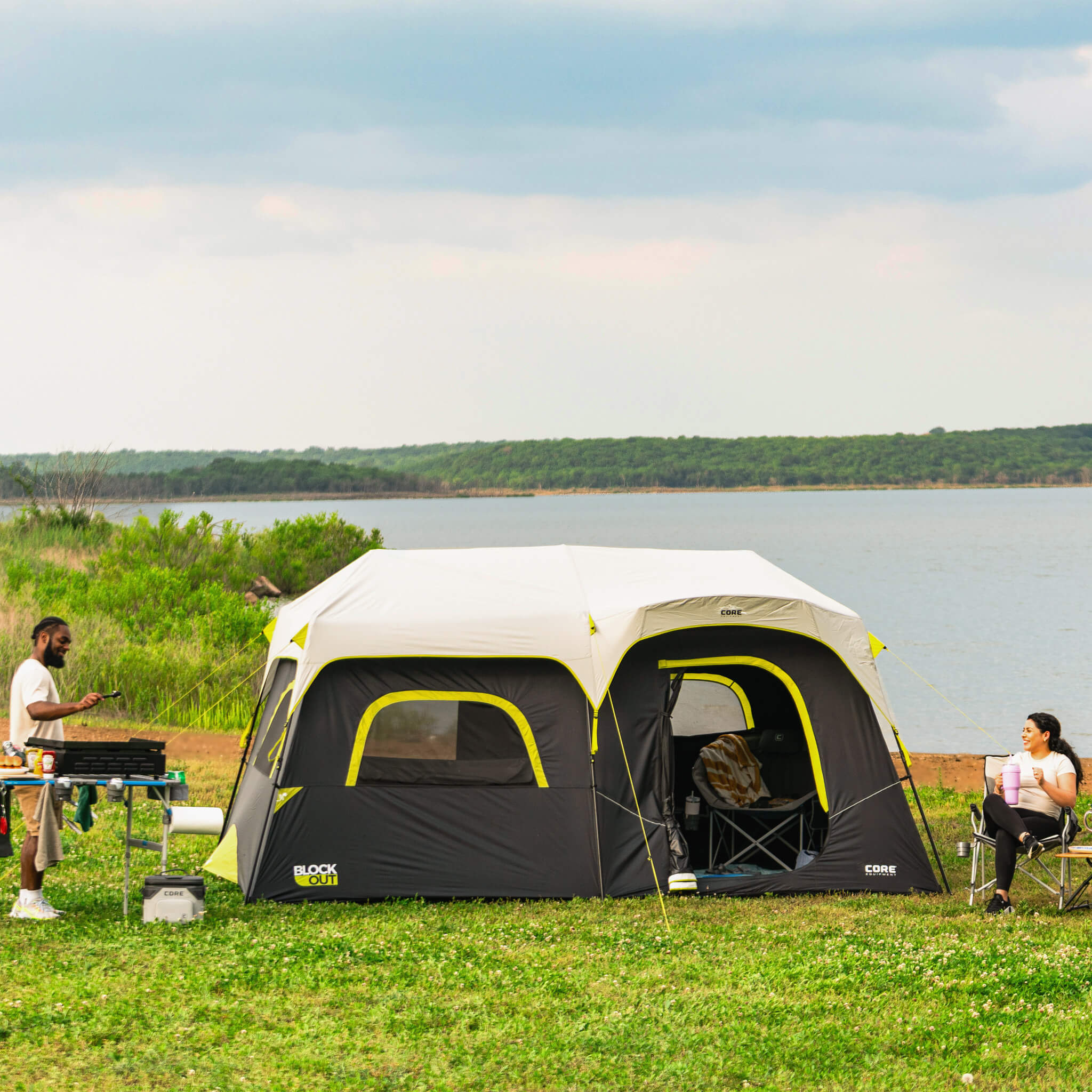 Family camping with CORE 9 person Blockout instant cabin tent set up by the lake, showing spacious design and dark interior.
