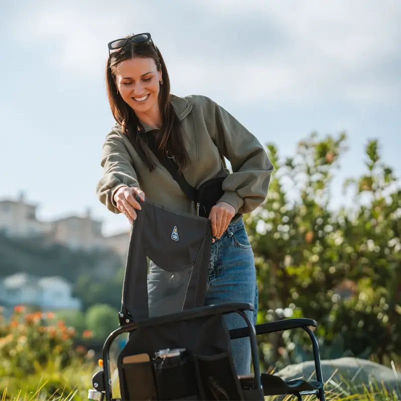 Woman sets up a black Adjustable Rocker chair outdoors, smiling under a clear sky