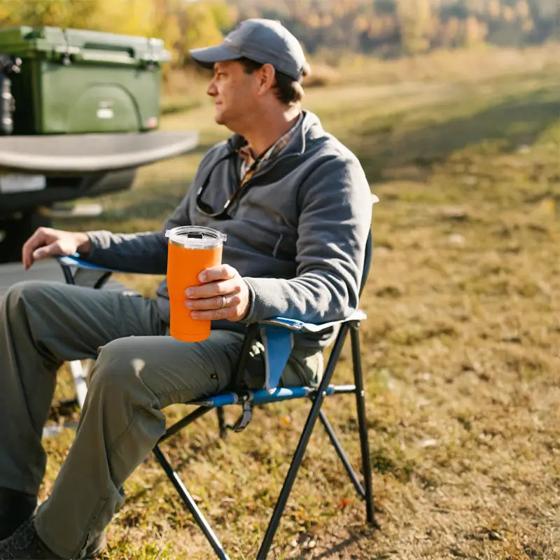 Man relaxing outdoors in a heathered royal Comfort Pro Chair, holding an orange tumbler.