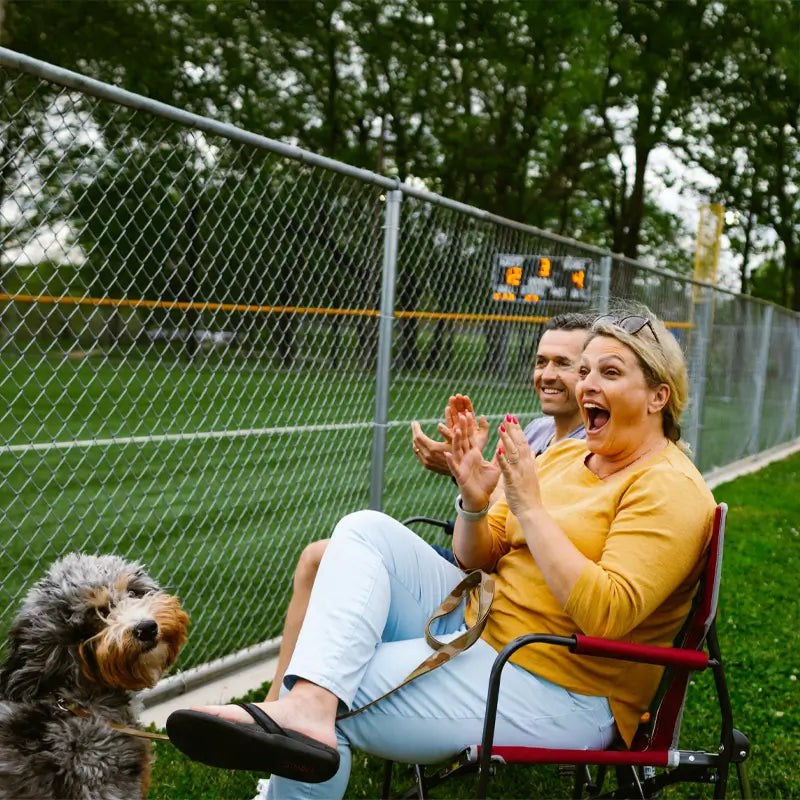 Woman cheering at a sports game while sitting on a cinnamon Freestyle Rocker with a dog beside her.