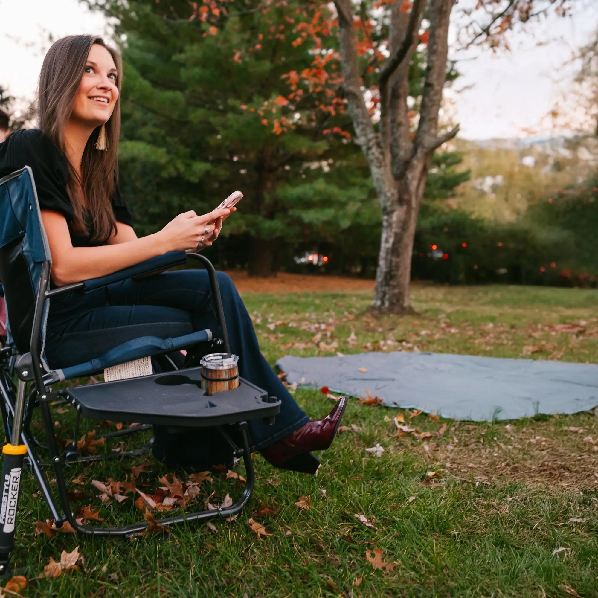 A woman smiling on her phone while sitting in an indigo freestyle rocker with side table. 