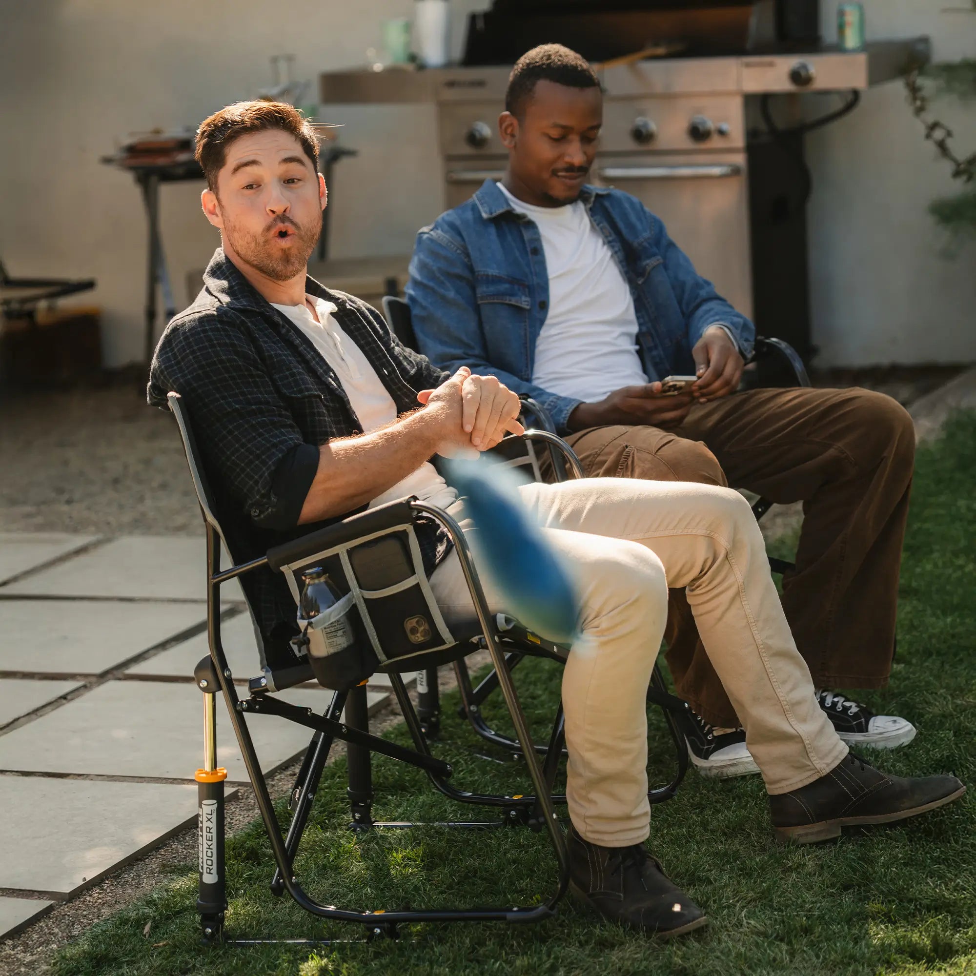 Two men watching people play corn hole in their black freestyle rocker xl chairs. 