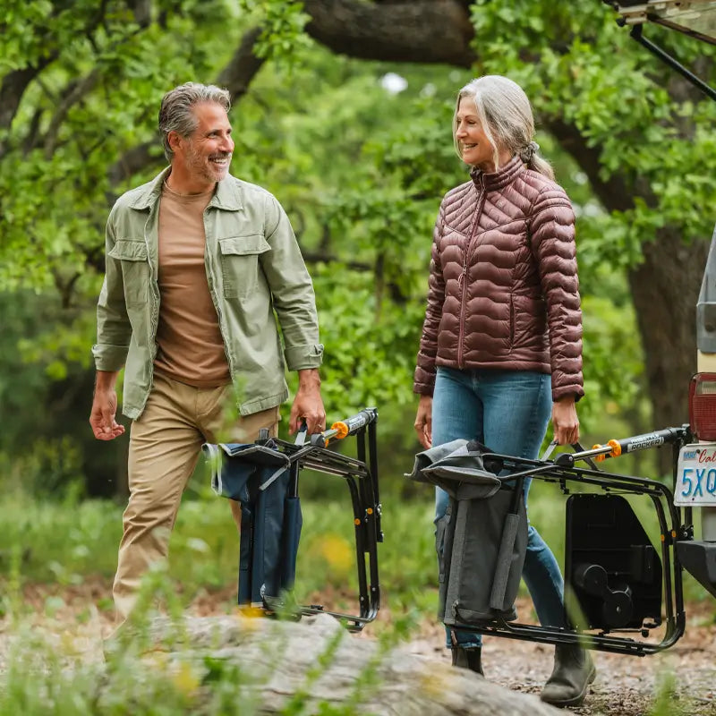 Man and woman smiling while carrying folded Freestyle Rockers through a forest trail.