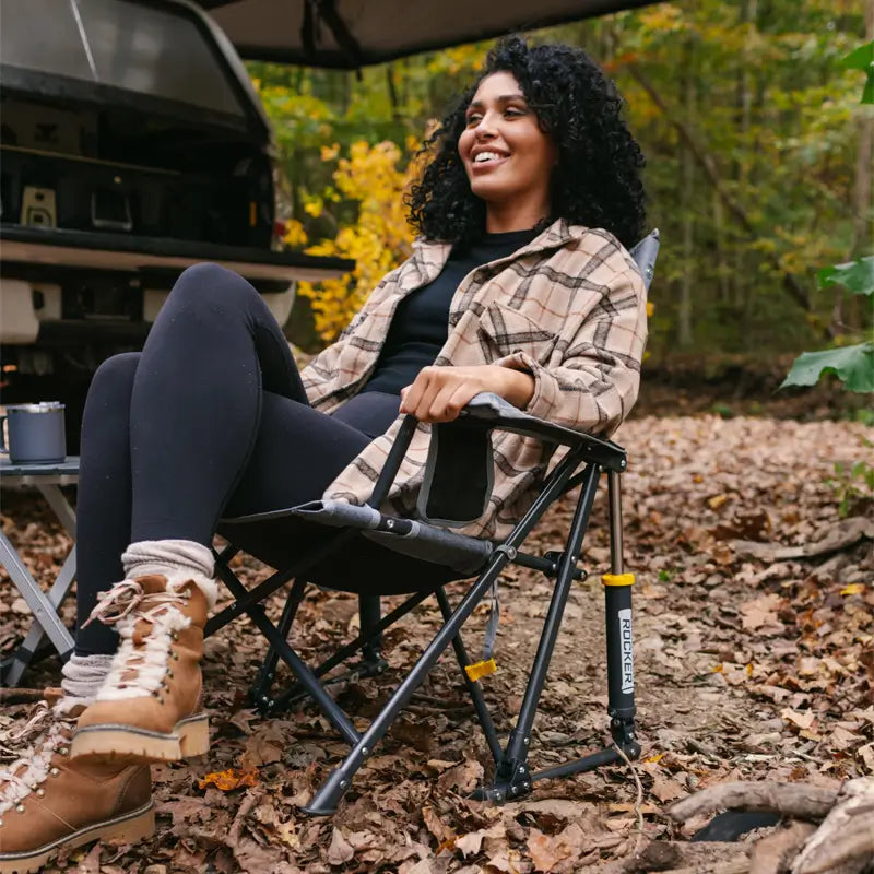 Woman relaxing in a heathered pewter Kickback Rocker chair at a forest campsite.