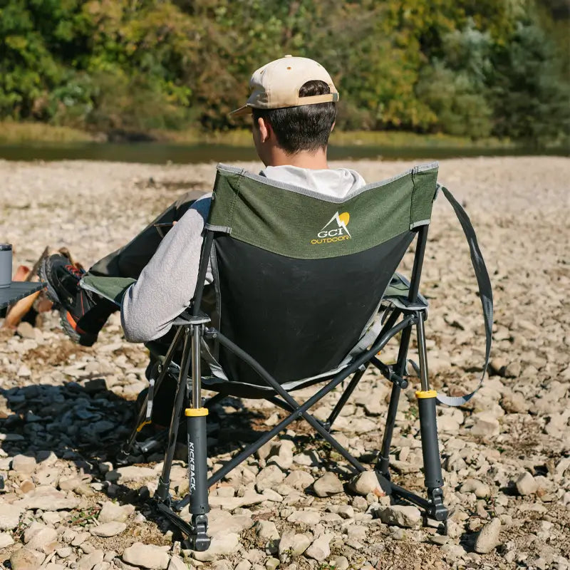 Person relaxing by a river in the heathered loden Kickback Rocker, back view showing GCI Outdoors logo.