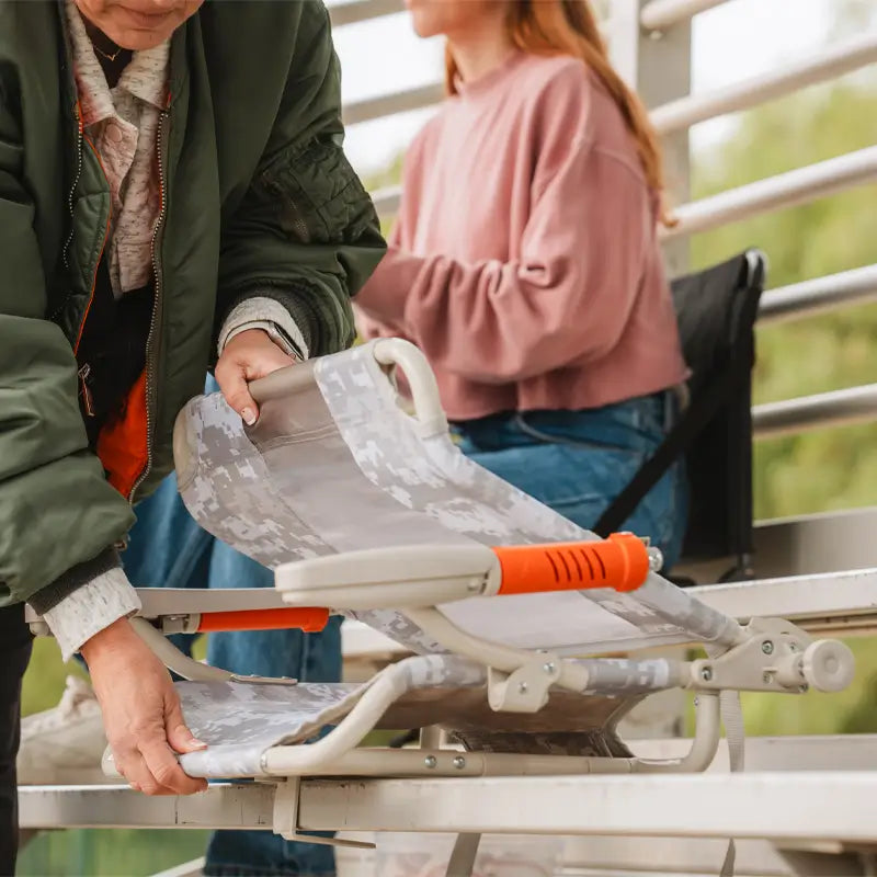 Woman locks the Snow Camo Stadium Rock-Cliner into place on bleacher bench.