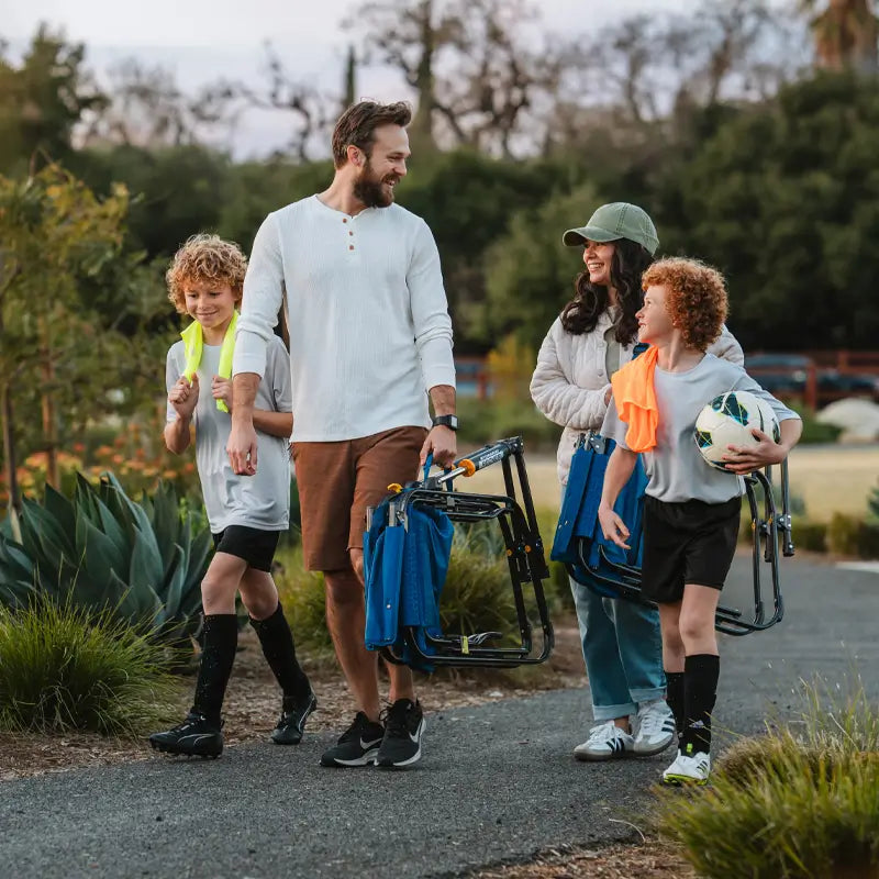 Family walking together on a path, carrying folded soft navy Stowaway Rockers after a soccer game.
