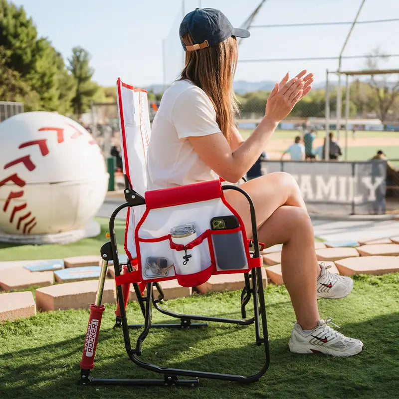 Person sitting on a red and white chair with a baseball theme at a sports event.