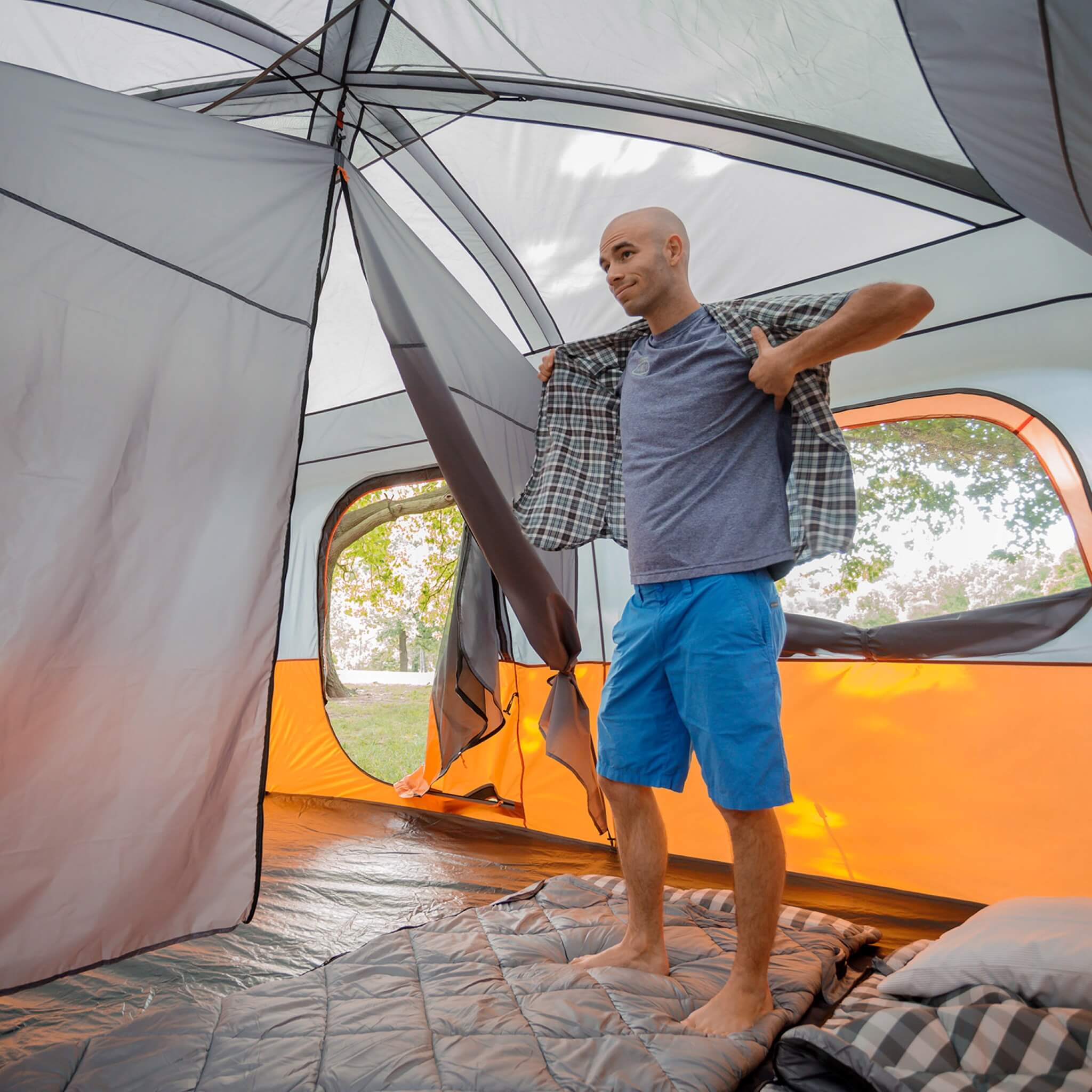 CORE 10 person straight wall cabin tent in orange and gray set up at a campsite with camper standing up inside the tent.