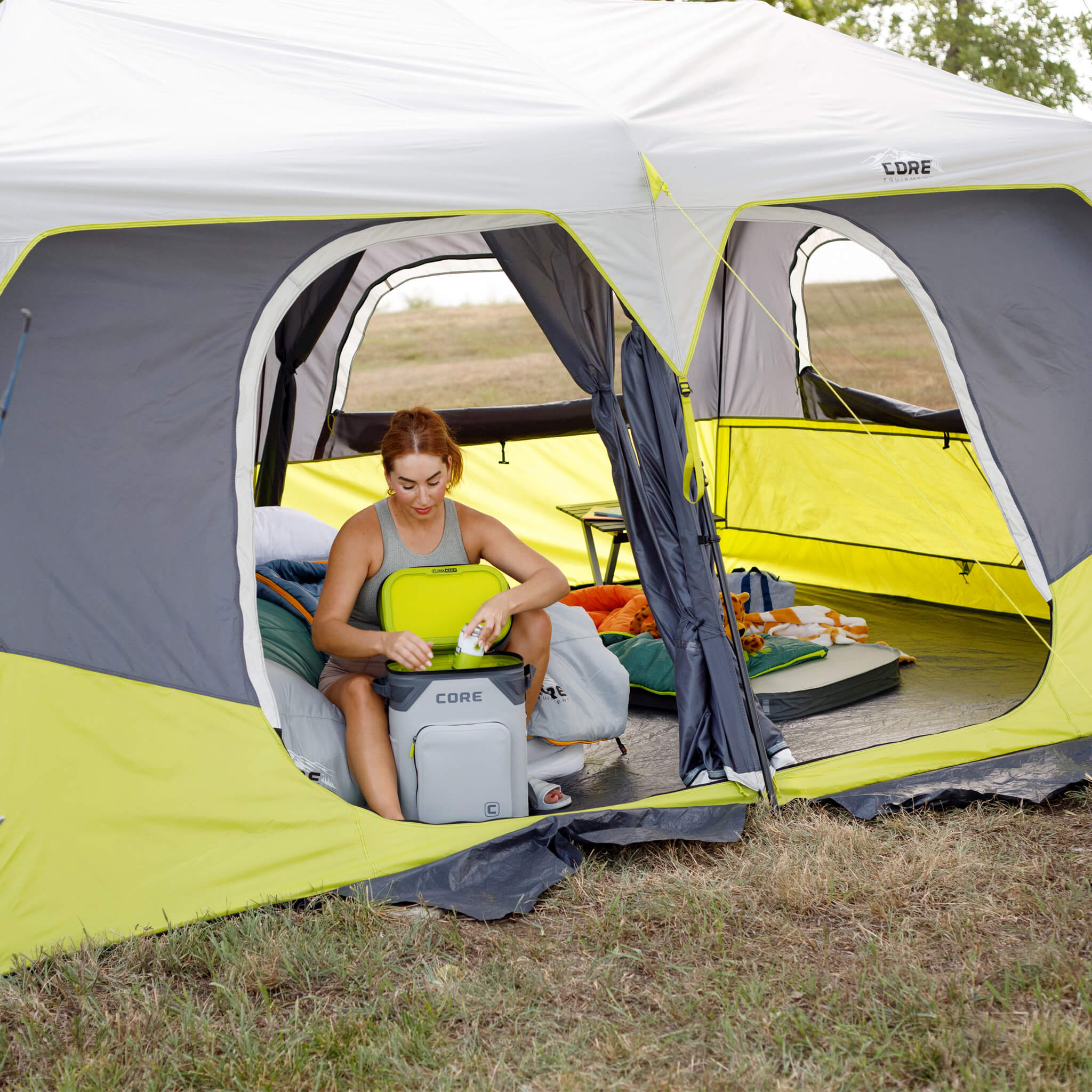 Camper sitting inside CORE 10 person instant cabin tent with CORE Climakeep cooler and large windows for ventilation and comfort.