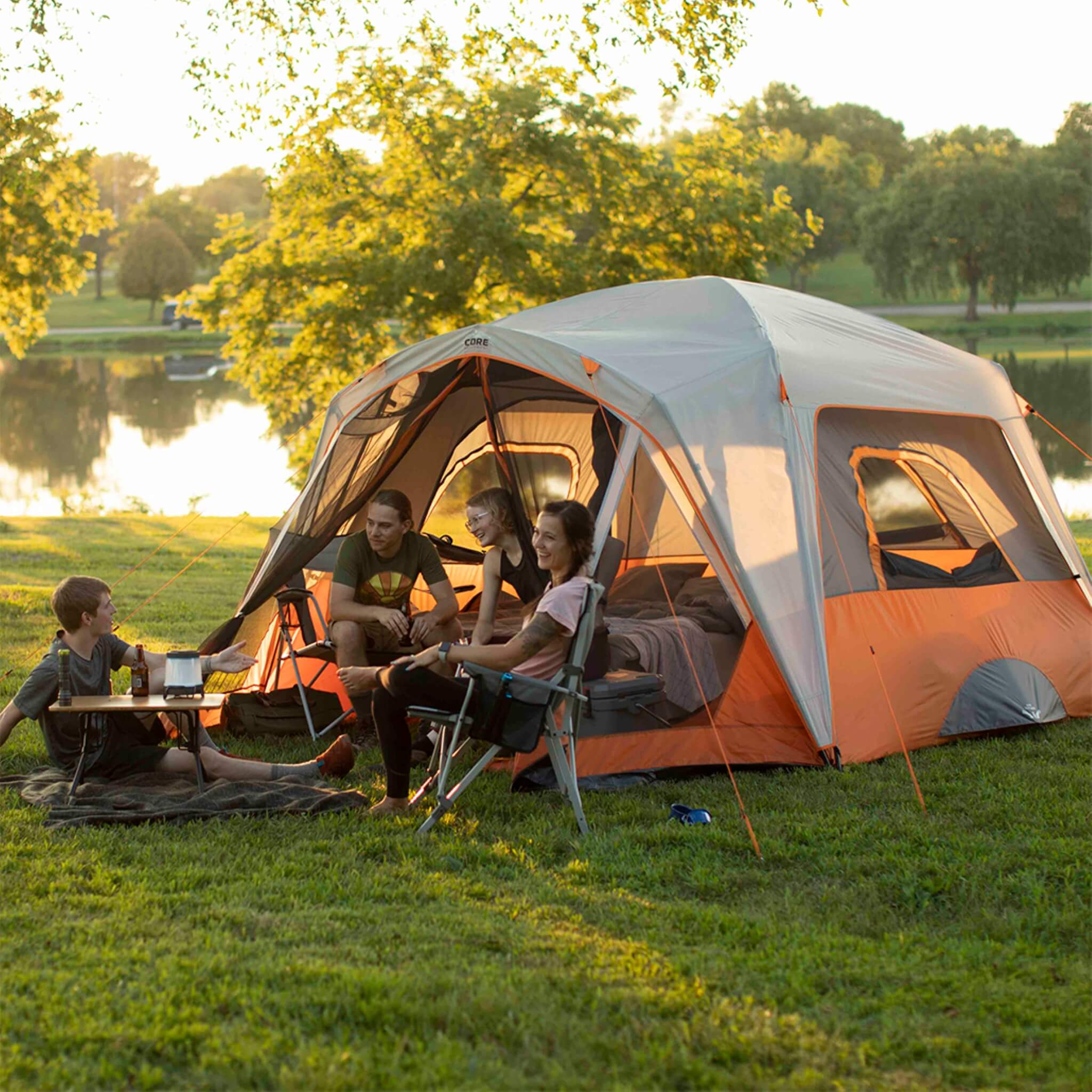 Friends hanging out next to a CORE 6 person straight wall cabin tent with screen room in orange and gray. 