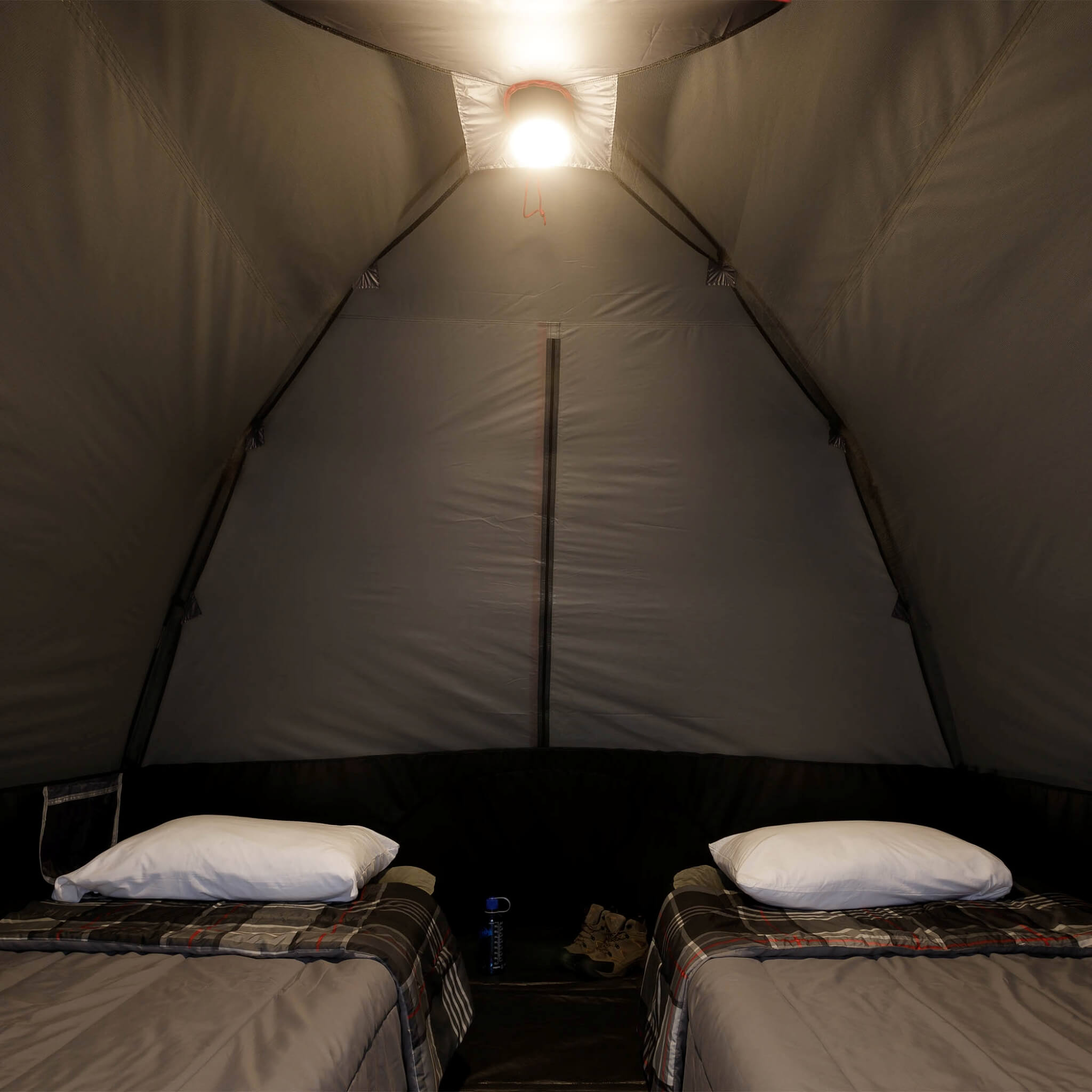 Inside view of CORE 6 person lighted dome tent with two cots, dark interior, and ceiling light on low mode providing overhead illumination.