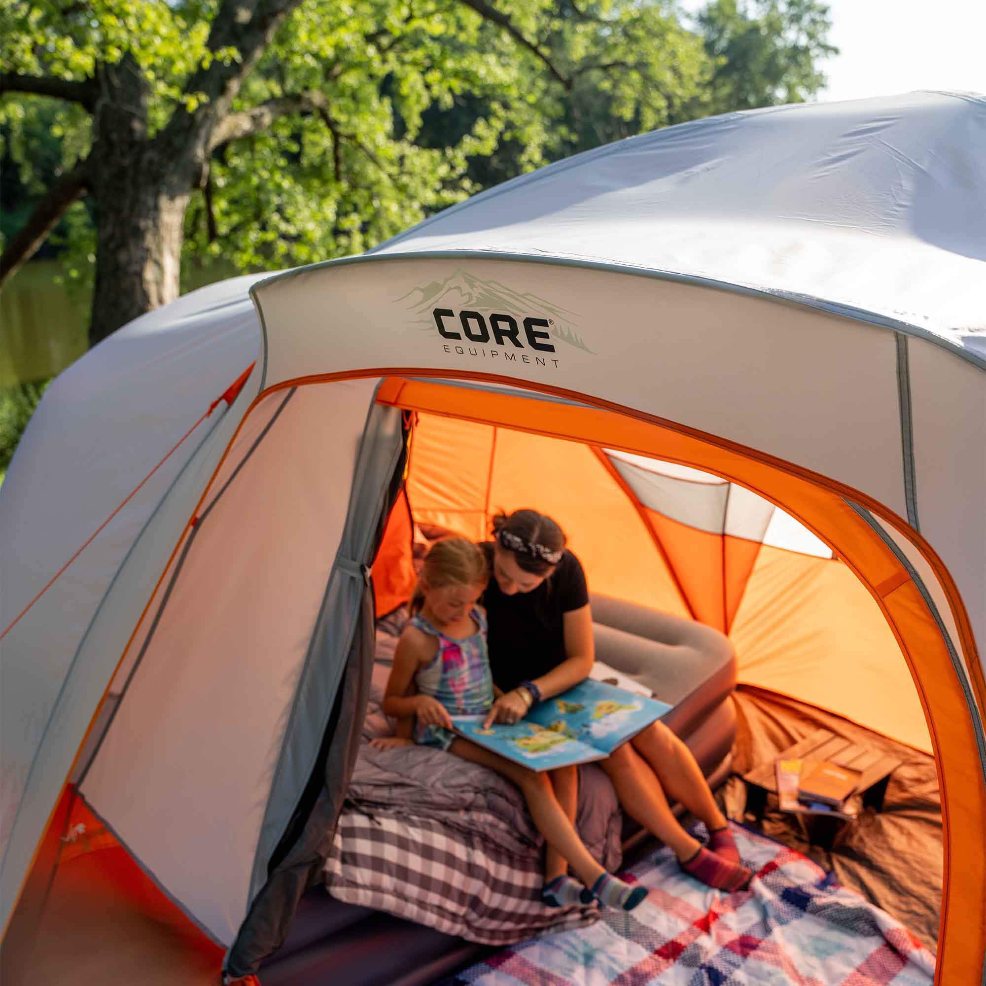 Mom and daughter are reading inside an orange and gray CORE 9 person dome tent.